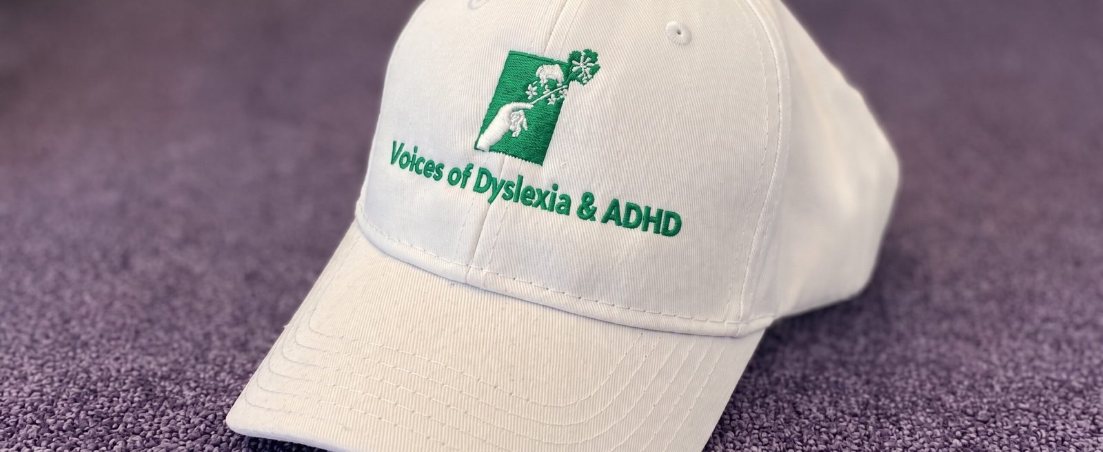Weisse Schirmmütze mit der grünen Aufschrift „Voices of Dyslexia & ADHD“