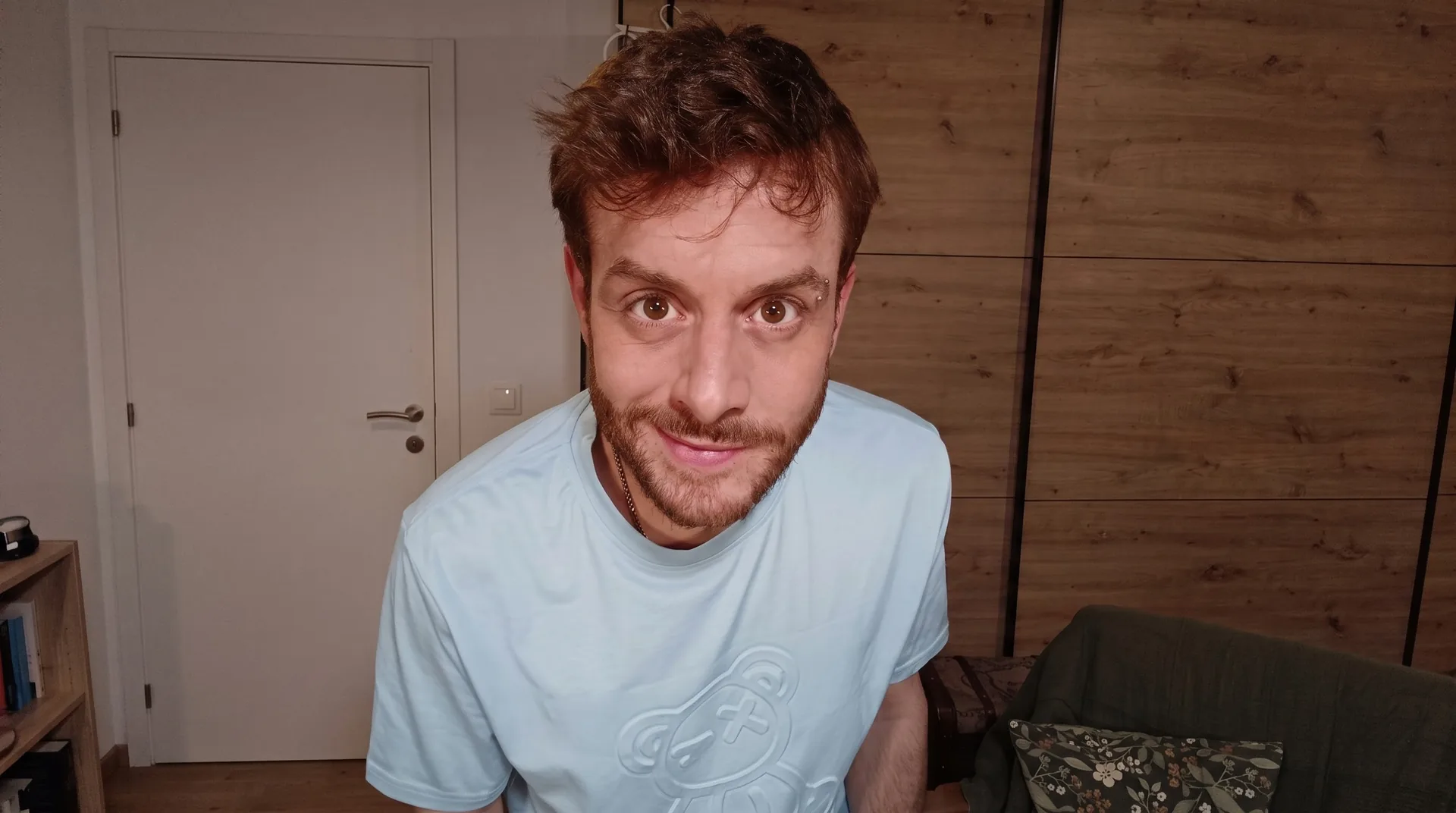 Luka Neww im hellblauen T-Shirt mit Teddy-Motiv beugt sich vor und lächelt verschmitzt in die Kamera